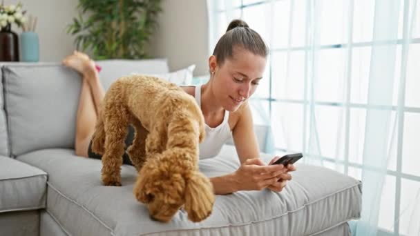 Köpekli beyaz bir kadın evdeki kanepede uzanmış akıllı telefon kullanıyor. - Video, Çekim
