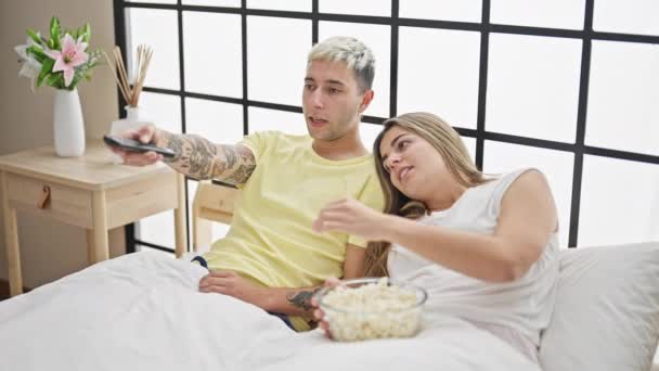 Beau couple regardant la télévision se battre pour la télécommande à la chambre - Séquence, vidéo