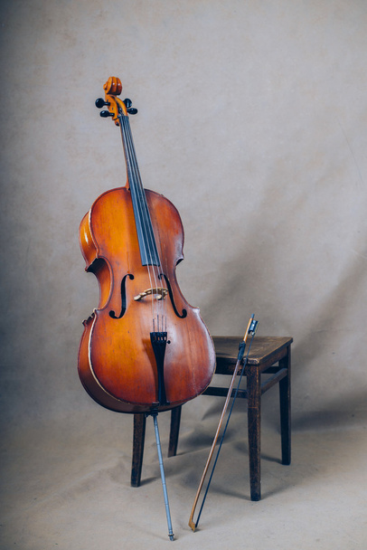 cello with bow near wooden chair on grey background - Photo, Image