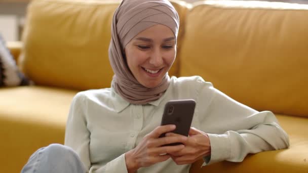 Giovane spensierata donna musulmana del Medio Oriente che scrive con gli amici online su smartphone, si riposa a casa, si gode i social media nei fine settimana, ritratto da vicino - Filmati, video