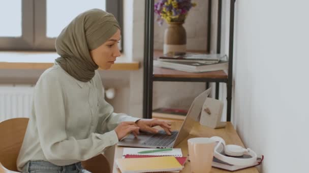 Concept d'économie de concert. Vue latérale de la jeune secrétaire occupée du Moyen-Orient portant le foulard tapant sur le clavier de l'ordinateur portable, travaillant à distance au bureau à domicile - Séquence, vidéo