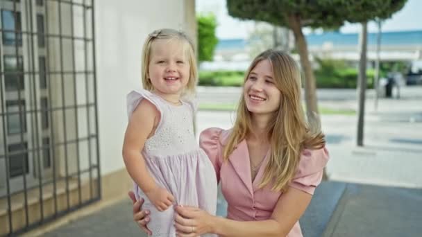 Joyful caucasian mum confidently standing on street, arms cradling her giggling daughter, both sharing a fun, positive outdoor moment in their favorite city. - Footage, Video