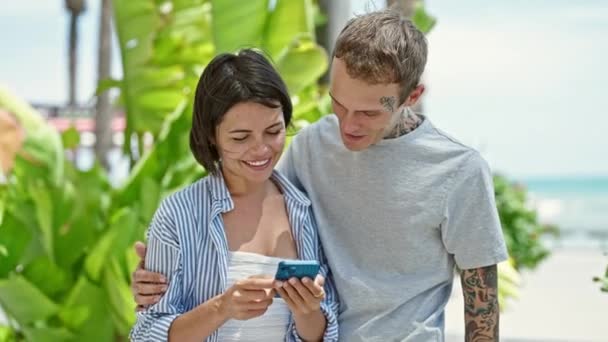 Hermosa pareja abrazándose entre sí utilizando el teléfono inteligente en el parque - Imágenes, Vídeo