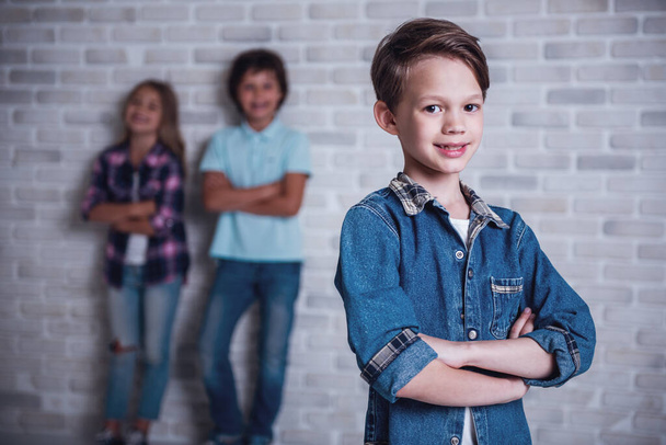 Niedliche Kinder schauen in die Kamera und lächeln, auf weißem Backsteinhintergrund. Ein Junge im Vordergrund - Foto, Bild