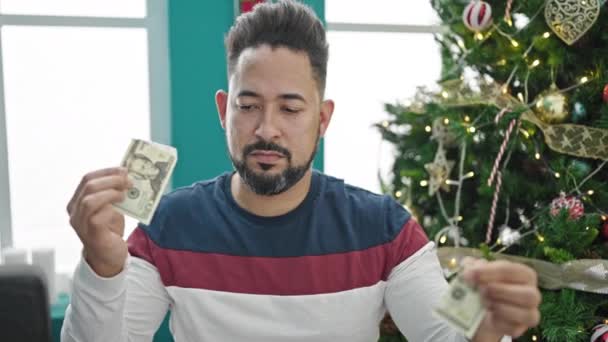 Fiatal latin férfi tör 20 dollár bankjegyek ünneplő karácsony otthon - Felvétel, videó