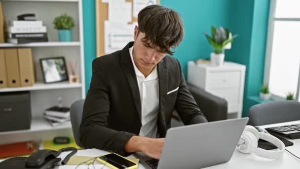 Genç İspanyol iş adamı ofiste dizüstü bilgisayar ve akıllı telefon kullanıyor. - Video, Çekim