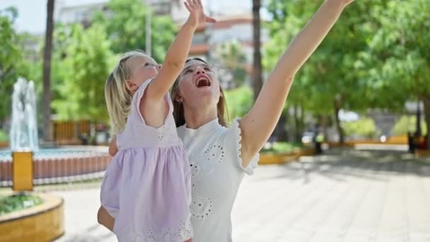 Cheerful mother confidently standing in the park, arms raised up, holding daughter up high, radiating happiness and joy - Footage, Video