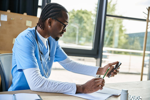 сфокусированный африканский американский врач в очках делает заметки и консультирует по телефону, телездравоохранению - Фото, изображение