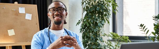 Веселый африканский американский врач со стетоскопом и очками улыбается и смотрит в камеру, баннер - Фото, изображение