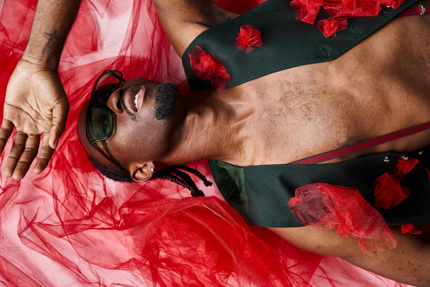 привлекательный модный африканский американец в солнечных очках в модном наряде, лежащем на полу, мода - Фото, изображение
