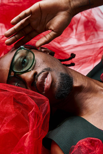 portrait of appealing african american man with red tulle fabric lying on floor, fashion concept - Photo, Image