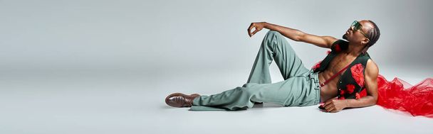 przystojny Afroamerykanin mężczyzna w stylowy strój z czerwonym tiulu tkaniny leżące na podłodze, sztandar - Zdjęcie, obraz