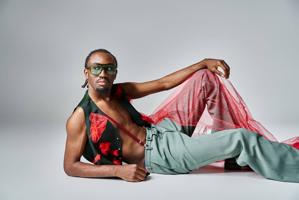 pohledný africký Američan v módní oblečení s červeným tylem tkaniny ležící na podlaze - Fotografie, Obrázek