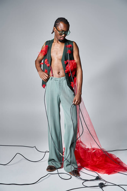 handsome african american male model with red tulle fabric posing in motion and looking away - Photo, Image