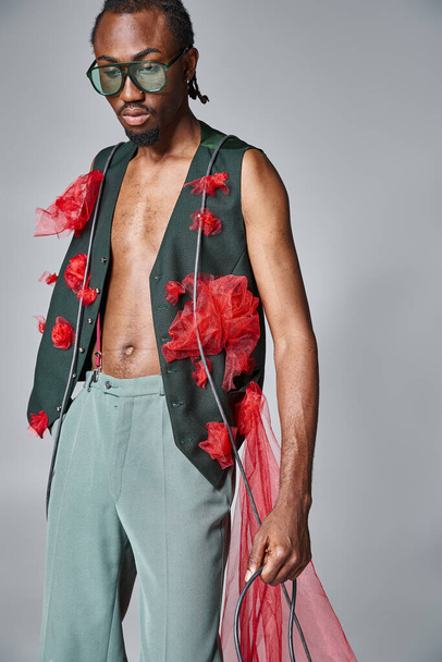 atractivo modelo masculino afroamericano con tela de tul rojo posando en movimiento y mirando hacia otro lado - Foto, imagen