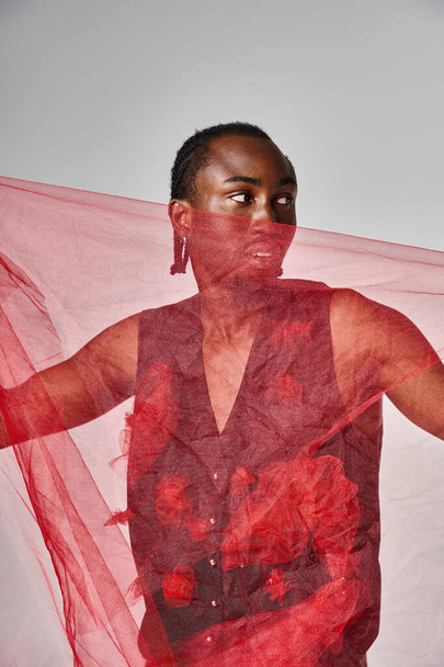 goed uitziende jonge Afrikaanse Amerikaanse man model poseren met levendige rode tule stof op grijze achtergrond - Foto, afbeelding