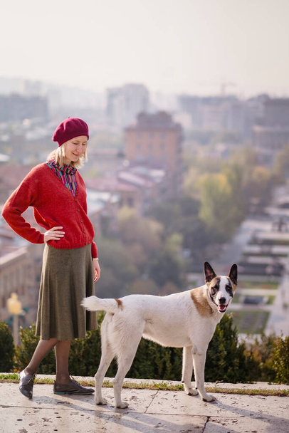 Une femme habillée dans le style des années 70 se tient avec un chien de rue. - Photo, image