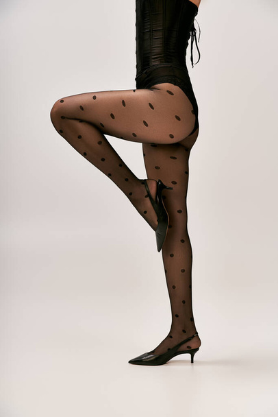 cropped shot of chic woman in corset, polka dot tights and high heels posing on white backdrop - Photo, Image