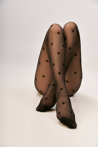 recortado disparo de mujer joven en negro lunares medias posando sobre fondo blanco, piernas cruzadas - Foto, imagen
