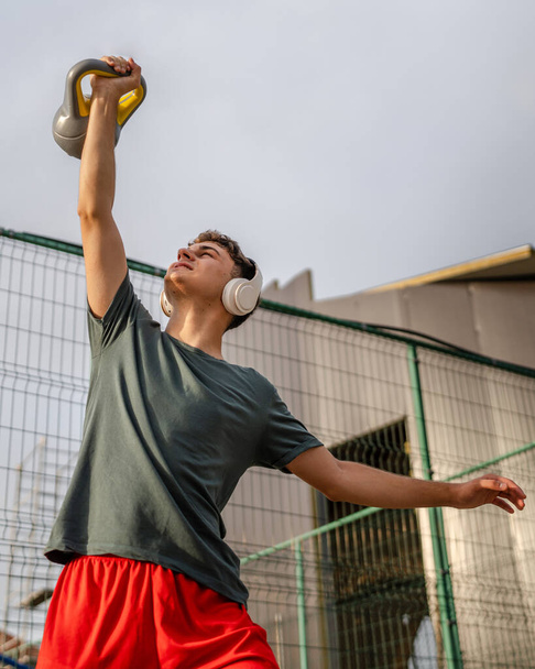 Um homem jovem caucasiano masculino adolescente stand ao ar livre no dia de treinamento com russo sino girya kettlebell peso exercício real pessoa cópia espaço - Foto, Imagem
