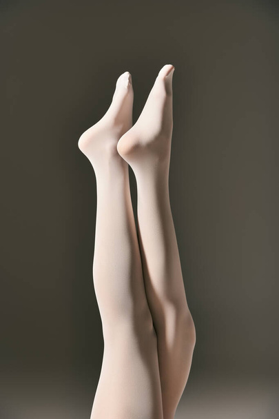 bijgesneden weergave van jonge vrouw in witte panty poseren met verhoogde benen op donkergrijze achtergrond - Foto, afbeelding