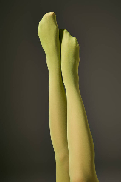 cropped view of young woman in green nylon tights on dark grey background, raised legs - Photo, Image