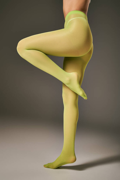 vista recortada de mujer joven en medias de nylon verde posando sobre fondo gris oscuro, punta del pie - Foto, imagen