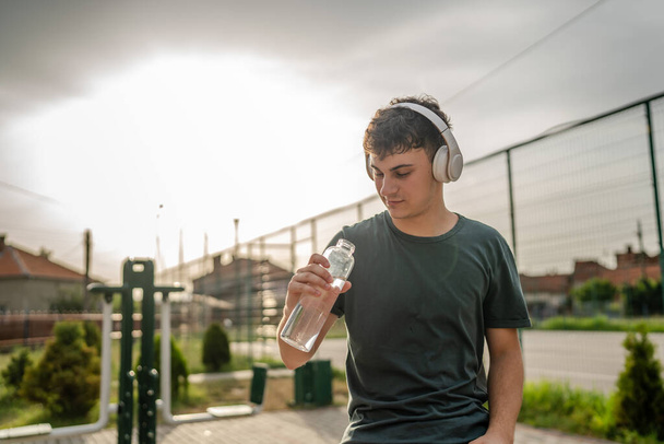 ein Mann kaukasischen männlichen Teenager halten Plastikflasche Wasseröffnung und bereiten sich auf das Trinken während des Trainings im Freien bei sonnigem Tag Flüssigkeitszufuhr und gesunden Lebensstil Konzept kopieren Raum - Foto, Bild