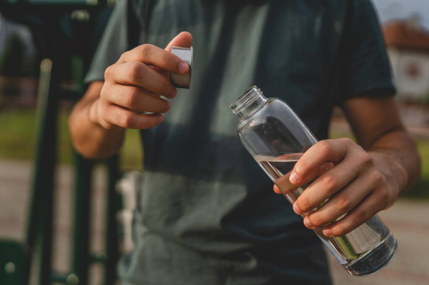 jeden mężczyzna kaukaski mężczyzna nastolatek trzymać plastikowe butelki wody otwarcia i przygotować się do picia podczas treningu na świeżym powietrzu w słoneczny dzień nawilżenie i zdrowy styl życia koncepcja przestrzeń skopiować - Zdjęcie, obraz