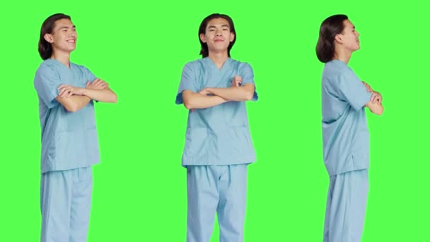 Barátságos nővér pózol a stúdióban magabiztosan, klinikai egyenruhát visel, és karját keresztbe tett zöld háttér. Az egészségügyi ágazatban dolgozó fiatal egészségügyi asszisztens. - Felvétel, videó