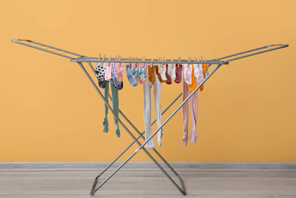 Чистая детская одежда висит на сушилке возле желтой стены - Фото, изображение
