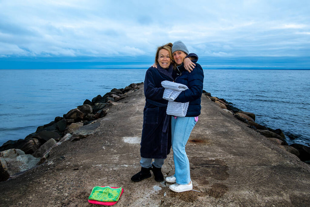 Bastad, Schweden Zwei Freundinnen auf einem Steg bereiten sich auf ein morgendliches Bad im kalten Meer vor. - Foto, Bild