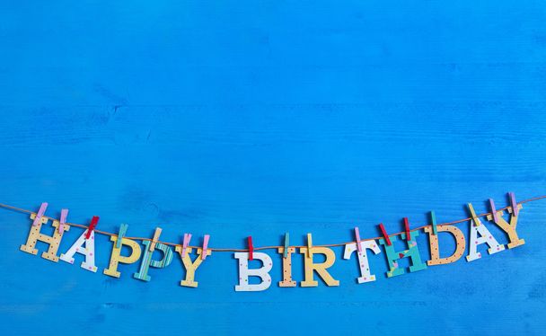 Blue background with colorful wooden hanging letters on a clothe - 写真・画像