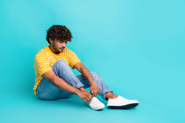 Full size photo of cool young person sit floor tie shoelaces empty space ad isolated on teal color background. - Φωτογραφία, εικόνα