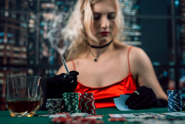 Богатая женщина носит вечернее красное платье, играет в покер, держит сигару. Игра в покер - Фото, изображение