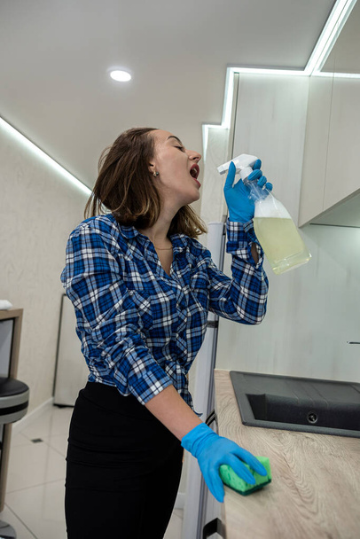 young woman in rubber gloves holds a rag and surface cleaner in the kitchen and cleans the room from dirt. the concept of cleanliness and order in the kitchen. maid - Photo, image