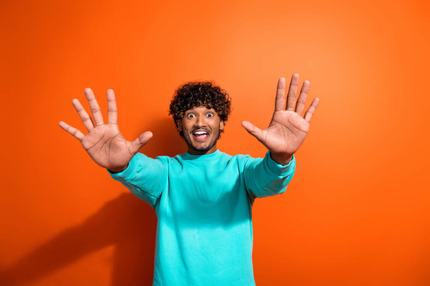 Portrait of funky youngster guy wearing trendy aquamarine sweatshirt raised palms ten amount sign isolated on orange color background. - Foto, immagini