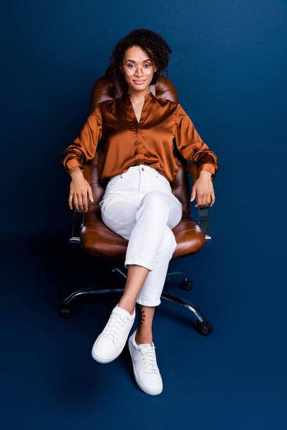 Vertical photo of attractive young woman sit armchair success wear trendy brown satin formalwear isolated on dark blue color background. - Fotoğraf, Görsel