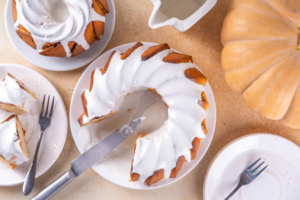 Homemade pumpkin bundt cake. Whole and slices of  sweet pumpkin round sponge cakes topped with sugar or white chocolate glaze icing, beige background copy space - Photo, Image