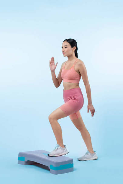 Vigorous energetic woman doing exercise at on studio short isolated background with cardio aerobic step workout. Young athletic asian woman dexterity and endurance training session concept. - Photo, Image