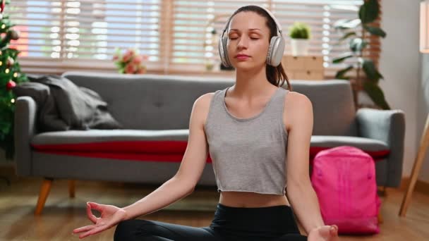 Beautiful young caucasian woman sitting in lotus position meditating at home. Healthy habit, mindfulness lifestyle concept. - Filmati, video