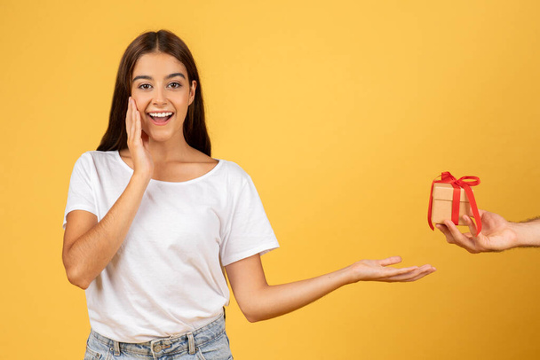 Smiling surprised young european woman take box present from man hand, isolated on yellow studio background. Gift to holidays, birthday and New Year, Xmas, Valentine day emotions - Photo, Image