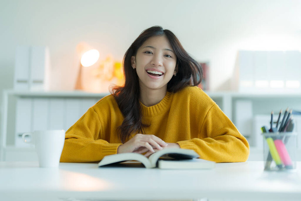 Egy fiatal nő könyvet olvas a könyvtárban, mosolyog és boldognak tűnik. - Fotó, kép