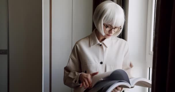 Jonge slimme vrouw met bril die thuis een boek leest. Stijlvolle vrouwelijke student flipping magazine, op zoek naar informatie om huiswerk te maken. Onderwijsconcept - Video