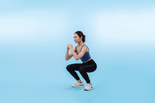 Vigorous energetic woman doing exercise. Young athletic asian woman strength and endurance training session as squat workout routine session. Full body studio shot on isolated background. - Photo, Image