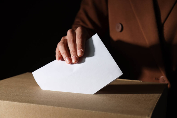 Scatola di voto in carta e mano con carta su sfondo marrone, primo piano - Foto, immagini