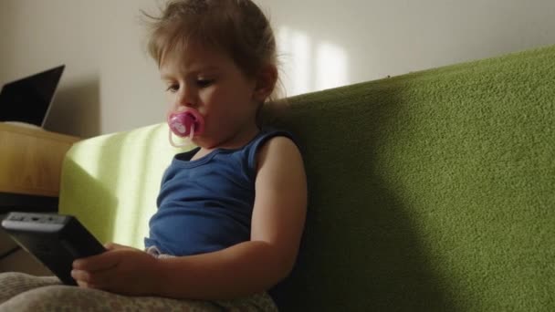 Весело милая девочка, играющая в приложение на гаджете для ПК видеоигры, сидя на диване дома. - Кадры, видео