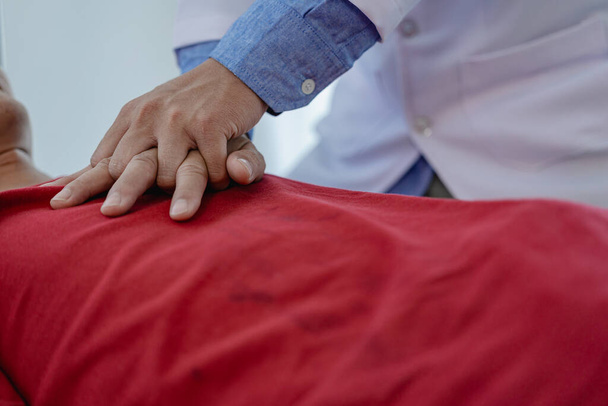 Close-up de um jovem asiático realizando RCP em um paciente deitado no chão. O paciente está em uma sala de cirurgia do hospital de emergência, onde o médico deve realizar RCP para estimular o coração. - Foto, Imagem