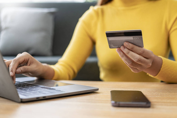 La mano de la mujer sostiene la tarjeta de crédito con el ordenador portátil y entra en el código de seguridad utilizando el teclado portátil, compras de tecnología en línea, pago con tarjeta de crédito - Foto, imagen
