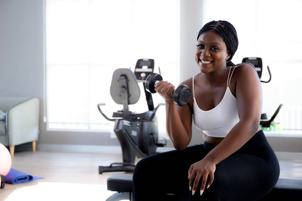 Молода чорна жінка тренує вправи або тренування з підйомним гантелі для культуристів з сильним фітнес-тренажерним залом, жінка практикує важку атлетику для сили м'язів і мотивації, спортивна концепція. - Фото, зображення